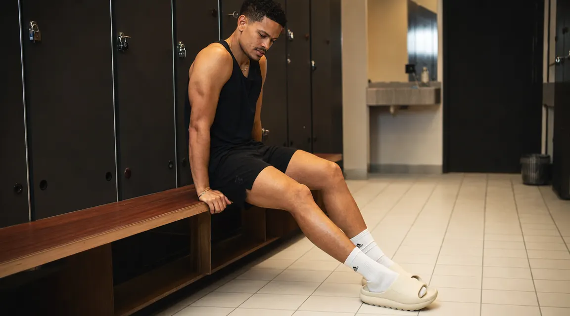 Person slipping on OOFOS OOriginal recovery sandals on a gym locker room bench after a workout